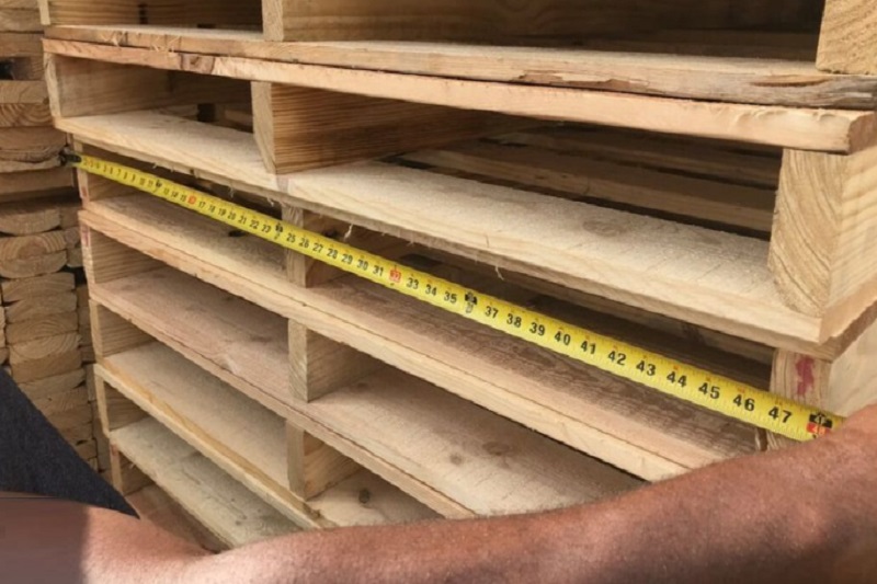 شخصی در حال اندازه گیری ابعاد پالت چوبی
